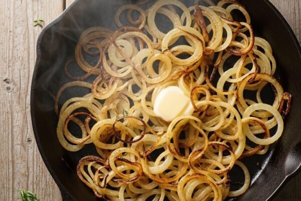 A cast iron skillet filled with perfectly caramelized onions, deep golden and glistening with butter, photographed overhead on a rustic wooden table with fresh thyme sprigs, representing the ultimate guide to making caramelized onions at home.