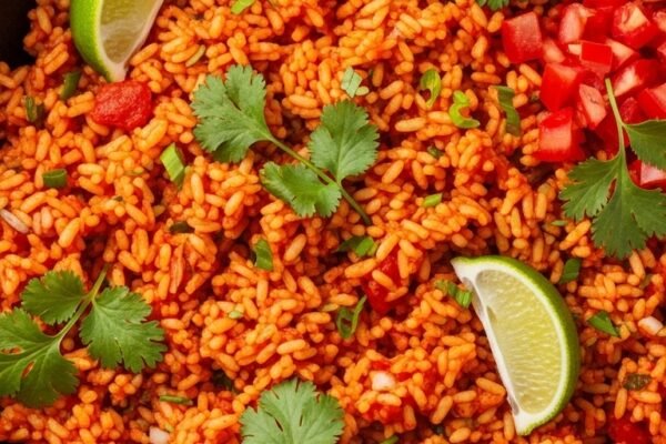 A perfectly cooked Spanish rice recipe in a rustic cast iron skillet with vibrant red-orange fluffy grains garnished with fresh cilantro and lime wedges, your ultimate guide to authentic flavorful homemade Spanish rice