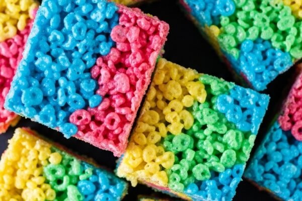 Colorful Fruity Pebbles Rice Crispy Treats cut into rainbow squares on a white plate, homemade dessert with bright cereal pieces.