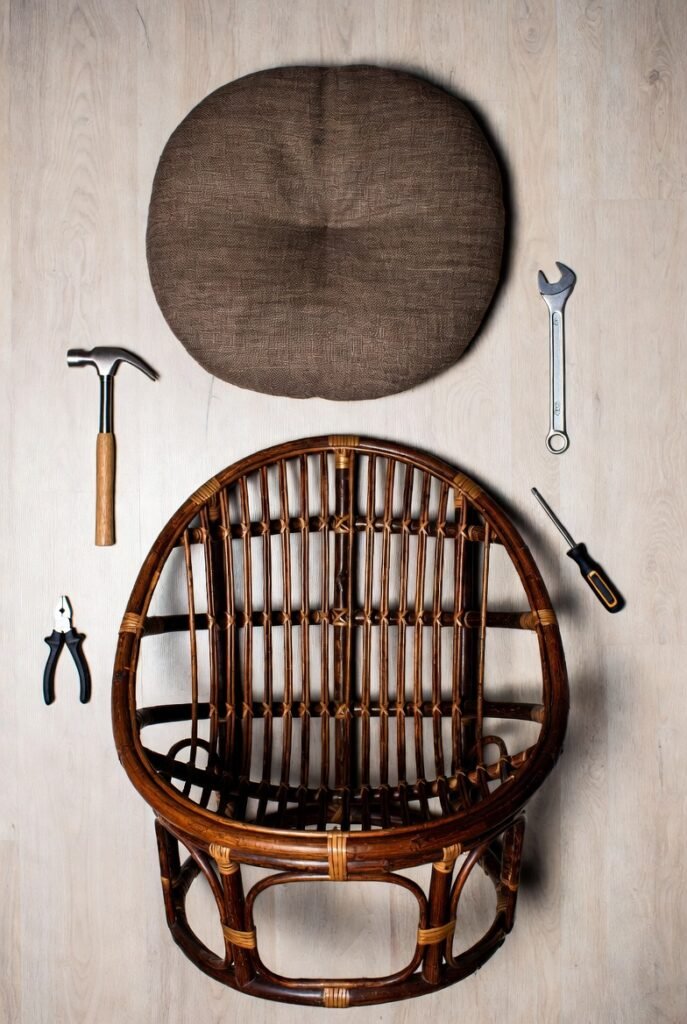 A step-by-step flat-lay of Papasan chair assembly — rattan base frame, bowl-shaped seat, cushion, and simple tools neatly arranged on a light wooden floor — top-down aerial photography, DIY lifestyle concept, clean and organized layout, warm neutral tones, satisfying and instructional feel.