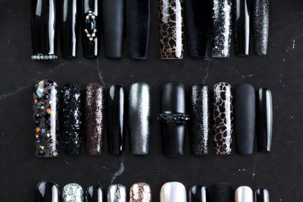 A stunning collection of 22 bold and wearable black nail designs featuring beautifully manicured hands showcasing a range of edgy yet elegant looks from classic glossy black and gold foil accents to matte velvet texture black lace stencils holographic speckles dichroic glass shifts and blood moon red underlays for the ultimate statement manicure inspiration.