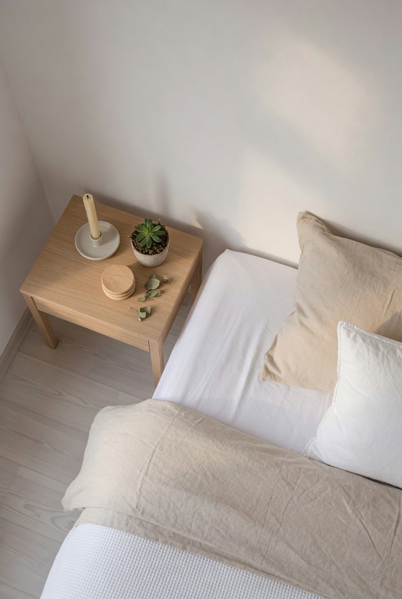 A serene minimalist bedroom with a low platform bed dressed in crisp white linen, a single potted plant, and warm morning sunlight streaming through sheer curtains, representing the ultimate guide to a bedroom minimalist transformation.